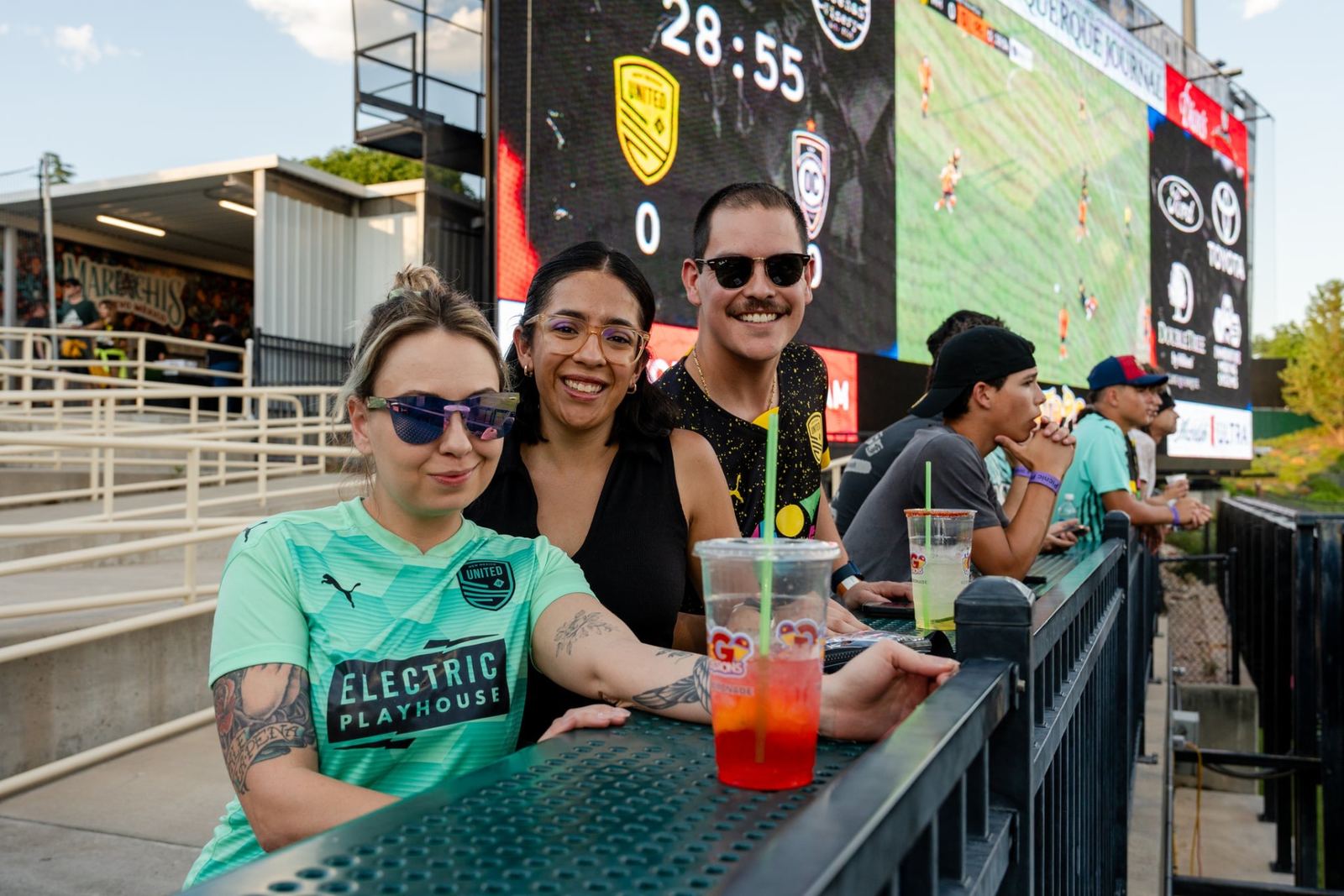 Better with Baron clients gathered at the rail beneath the stadium scoreboard during a New Mexico United match in Albuquerque.