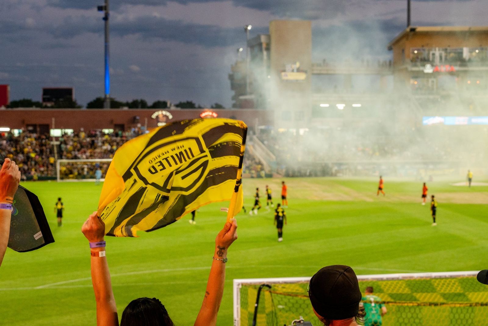 A New Mexico United flag waving over the pitch at dusk during the Better with Baron client appreciation game night.