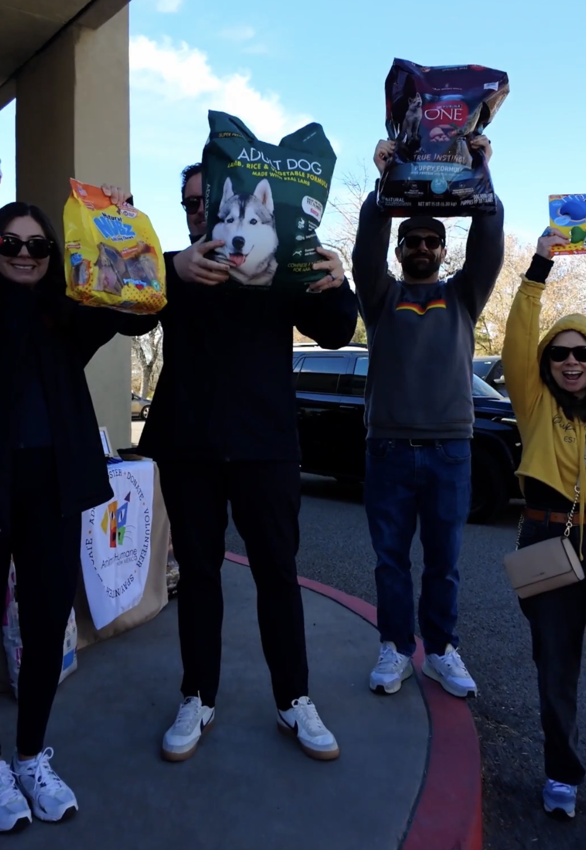 Better with Baron team holding donated bags of dog food overhead for Animal Humane New Mexico